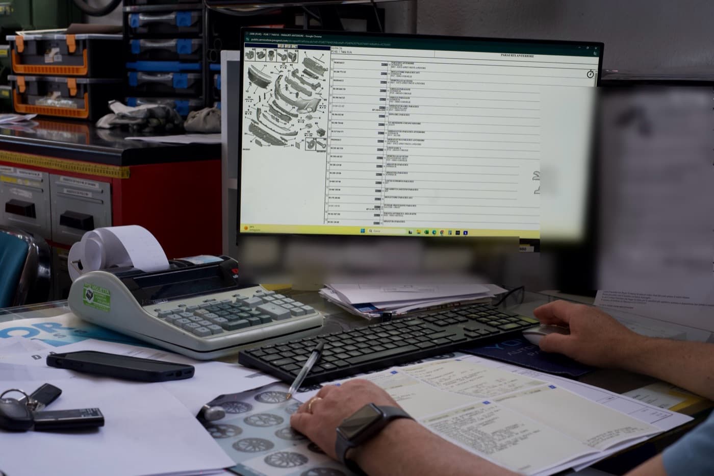 La verifica del ricambio sui portali ufficiali, con l'esploso dei componenti a schermo e il libretto sul banco